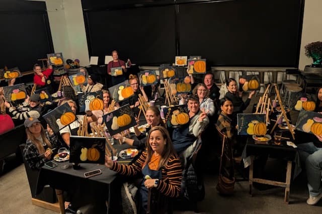 A paint night group holding up their finished pumpkin paintings