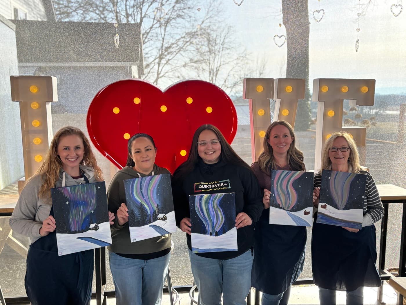 Five guests holding the canvases they painted at an Uplift community paint night